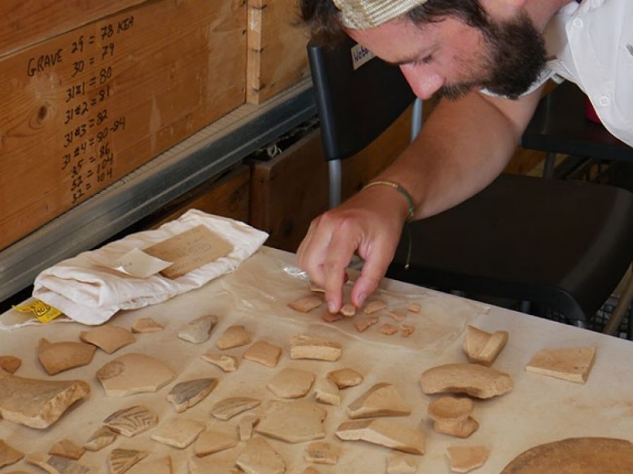 Graduate Student Theo Nash examining pottery shards on a table. at the Kea dig site in 2024