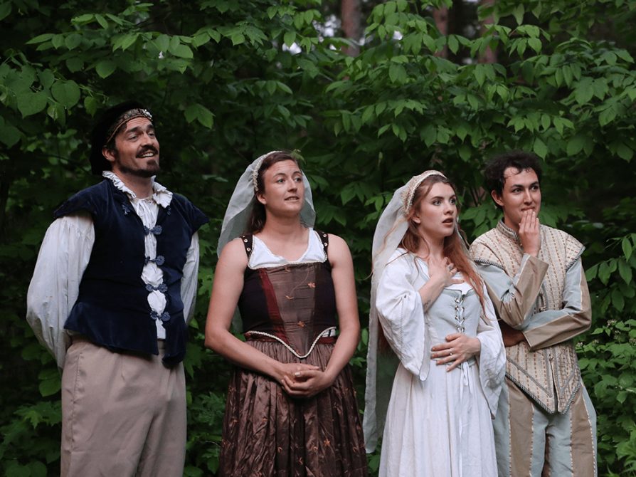 Performers dressed in Shakespearean clothes react to something happening in the production.