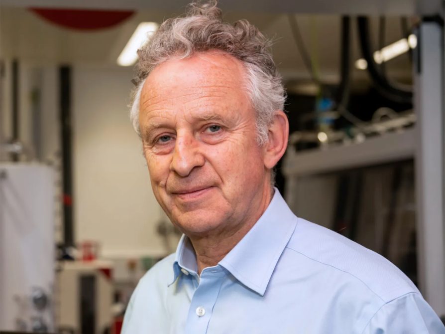 an individual in a blue collared dress shirt with gray and white hair with a smile