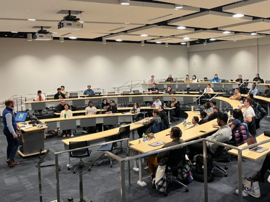 Mark Stephenson presents to a group of listening students in a seminar classroom with tiered rows in a semicircle shape.