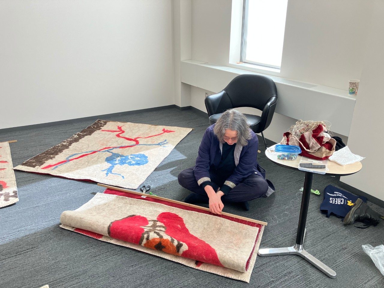 Gluklya threading a tapestry to be hung.