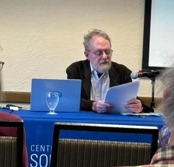 David Lelyveld sitting at a blue table reading from a paper
