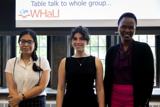 Three presenters stand facing the camera and smiling