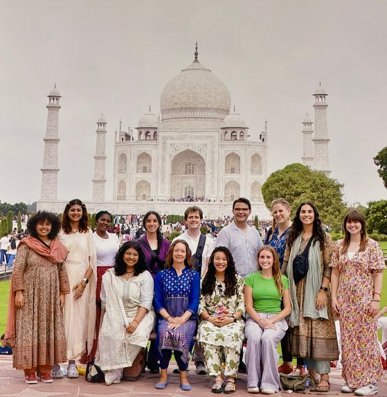 A group of people in colorful, traditional Indian clothing are posed in front of the Taj Mahal 