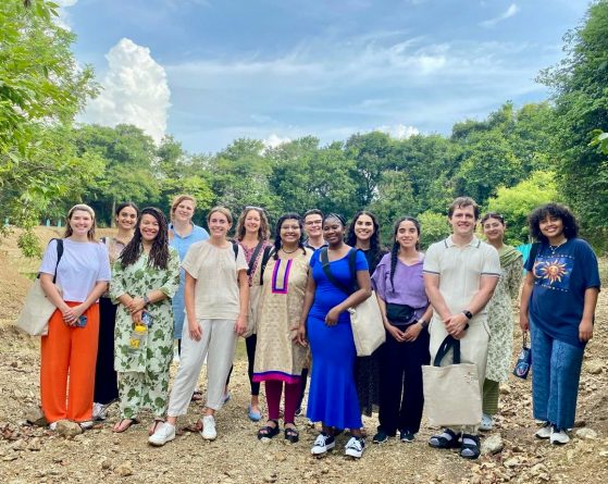 A large group of people pose together outside in of a tree lined open field