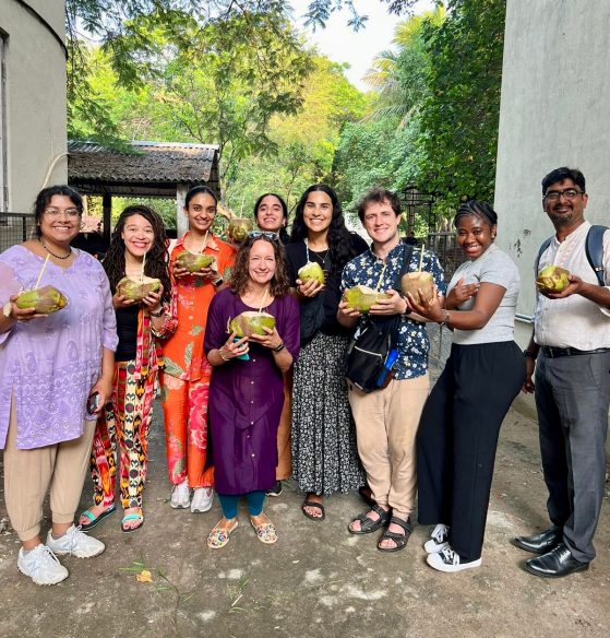 Group photo of nine people standing outside holding coconuts and smiling