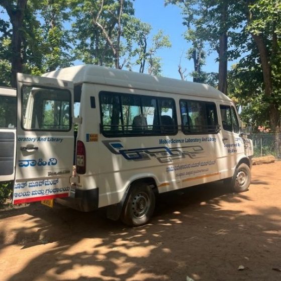 A white mobile health van is sitting on a dirt road with open back doors