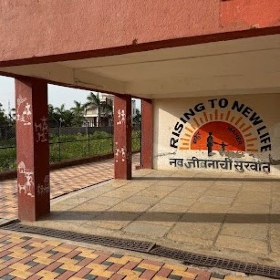 An empty building patio with a mural of the sun and two figures that says "Rising to New Life"