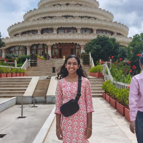 Vishalakshi Meyyappan stands in front of an ornate building while smiling