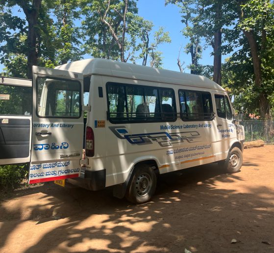 A white mobile health van is sitting on a dirt road with open back doors