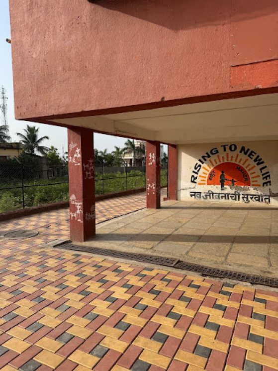 An empty building patio with a mural of the sun and two figures that says "Rising to New Life"