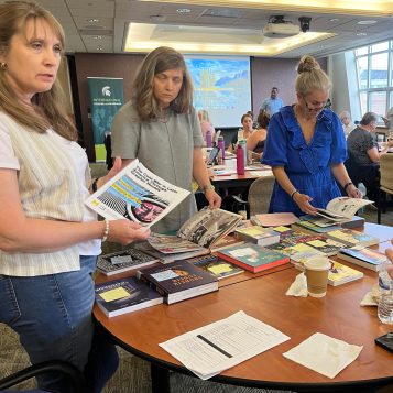 Three individuals are standing around a table looking at various graphic novels