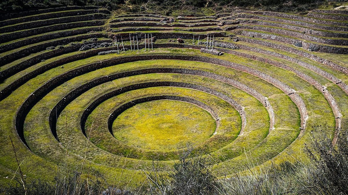 A circular terraced Inca ruin with green grass and stone walls, set into a hillside.