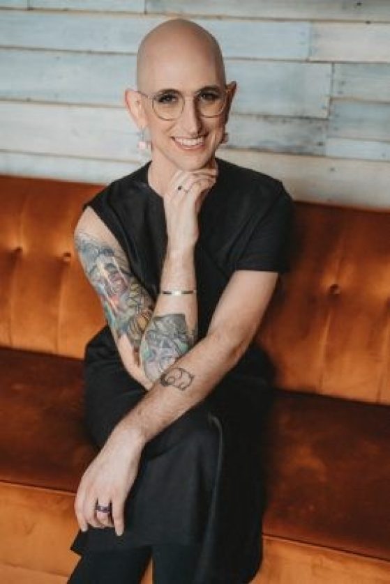 Image of Toni, wearing all black, glasses, sitting on a couch