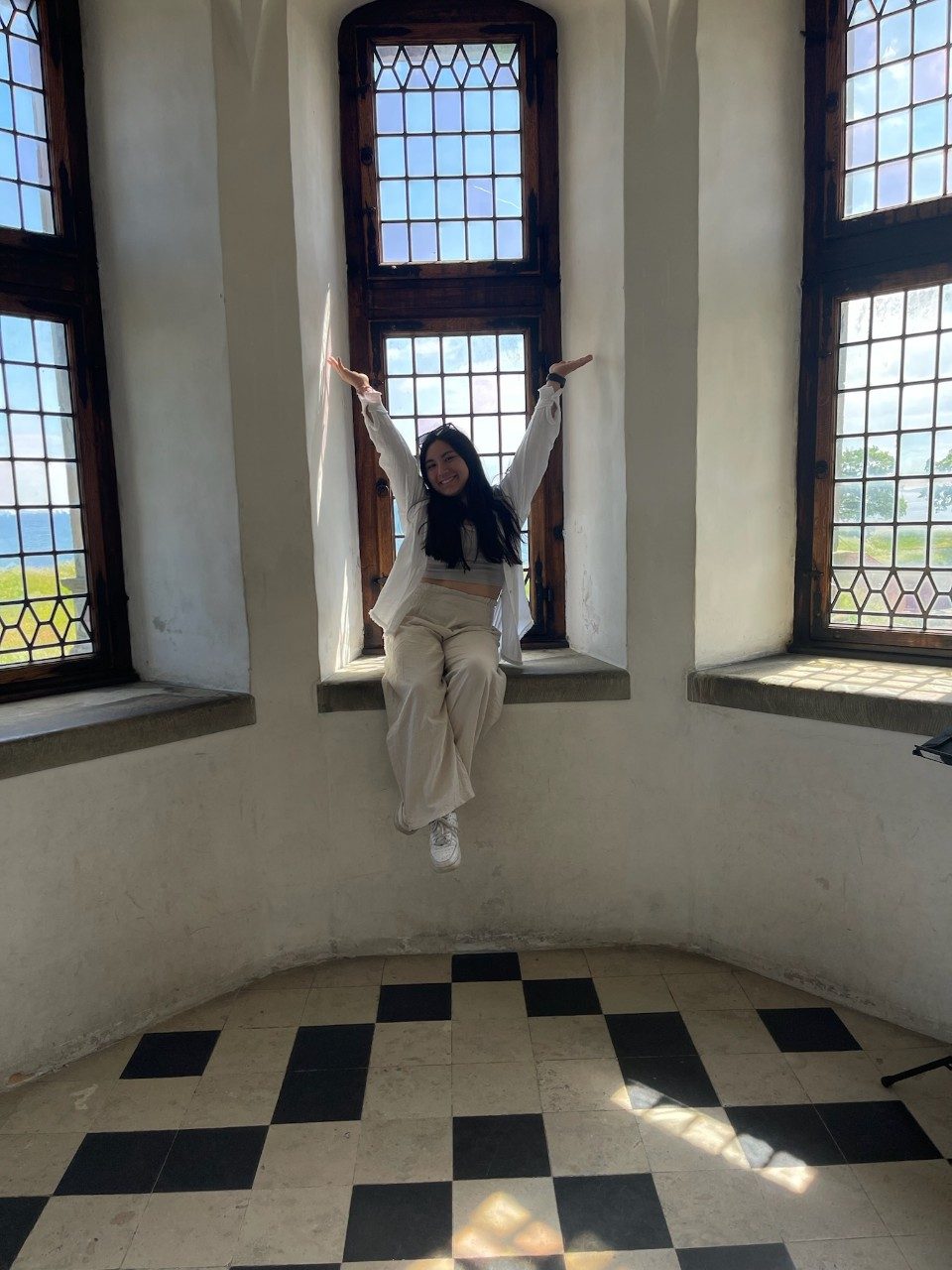 Nicole sits smiling on the interior window ledge of Helsingør Castle with her arms above her head in a Y pose.