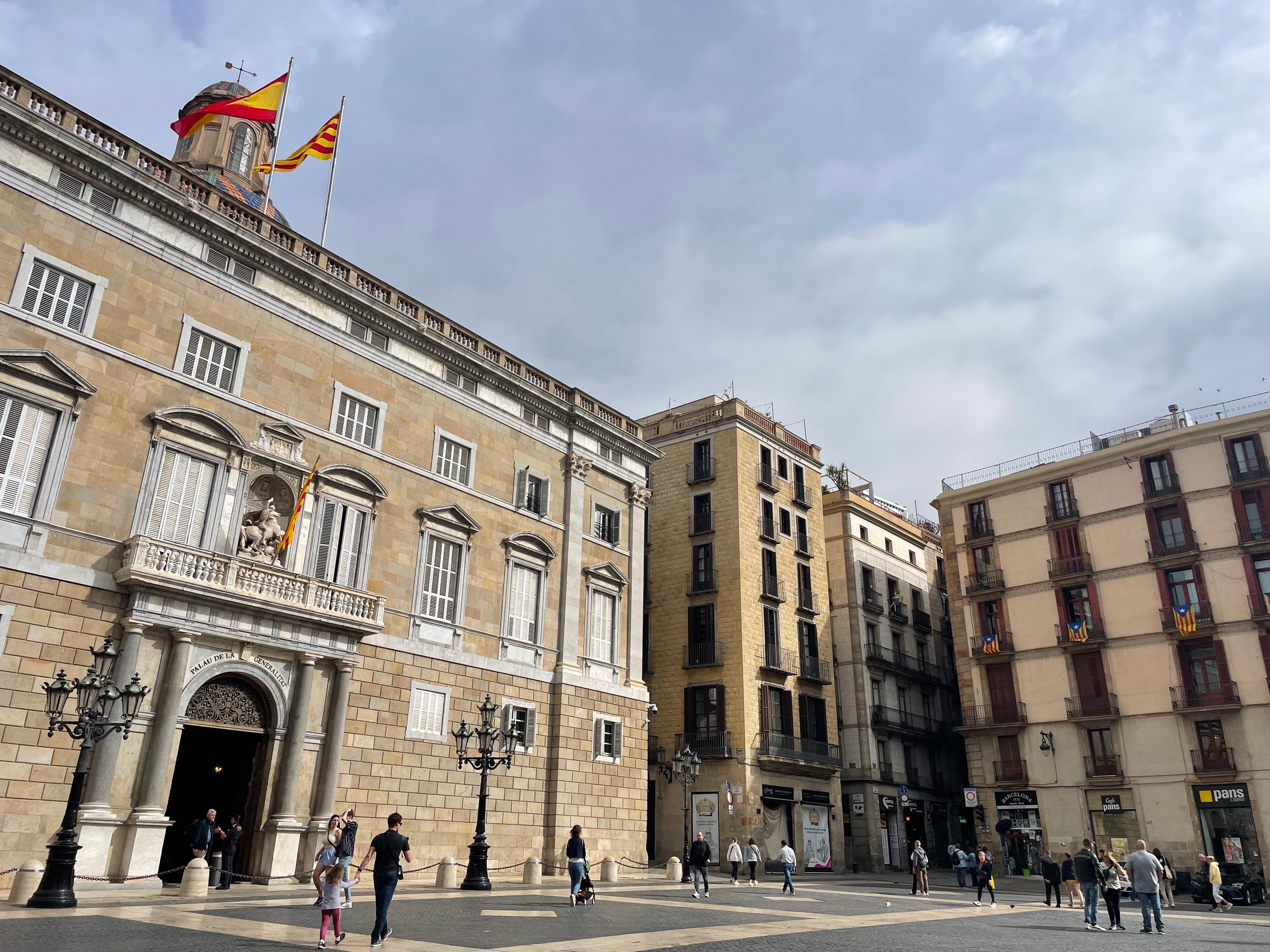 Contrasting Spanish and Catalan flags atop building in Barcelona.