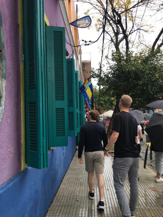 A vivid, colorful building with bright green shutters is being passed by two persons.
