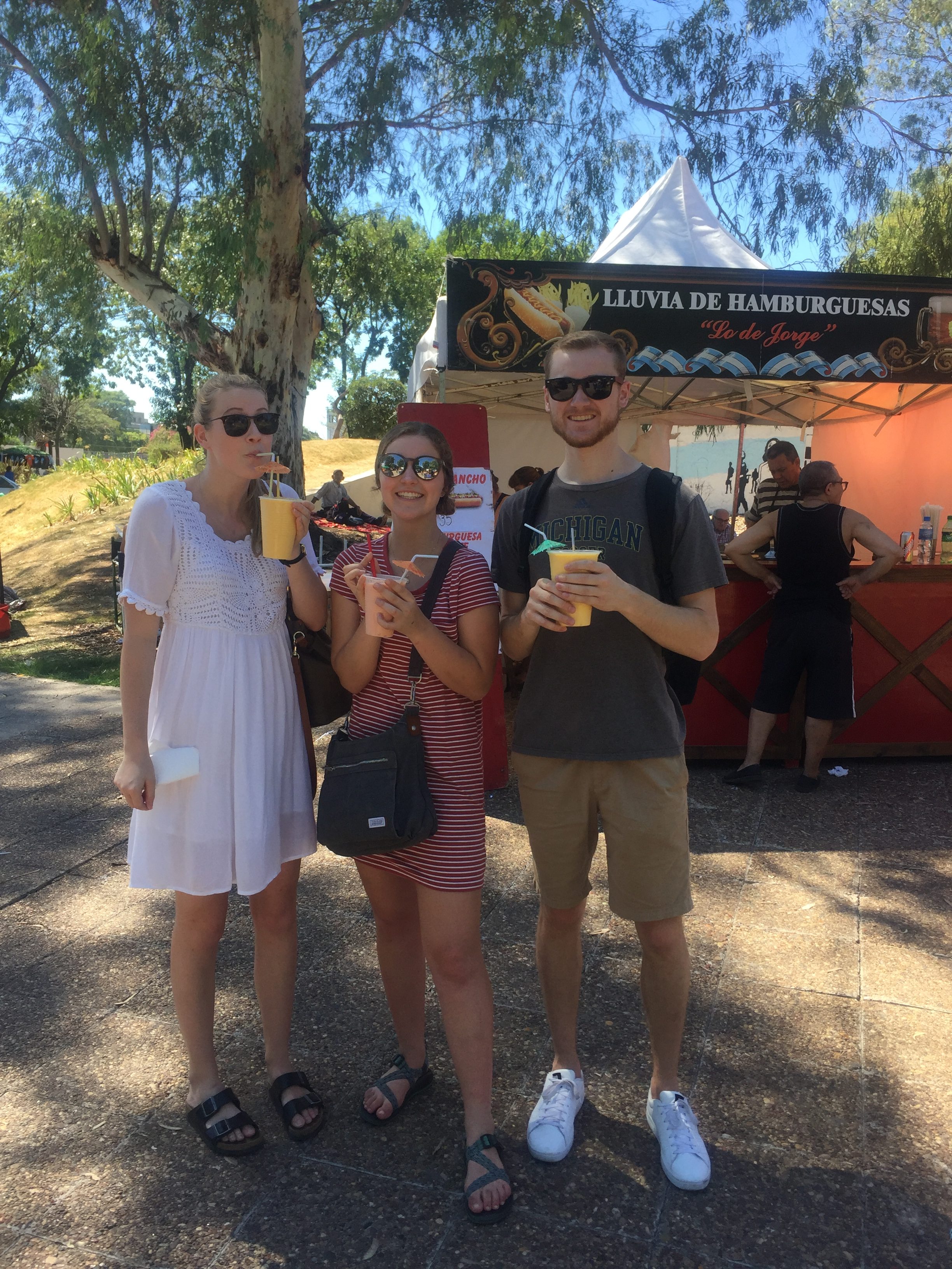 Outside, three students are posing with drinks in front of a refreshment stand.