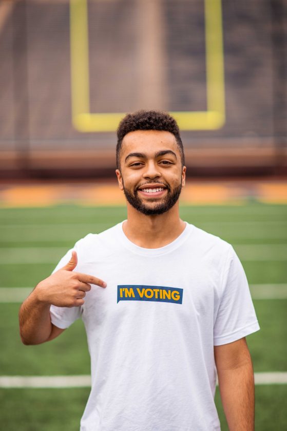 Adian Sova smiling and pointing to his t-shirt which states "I'm voting"