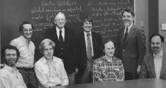 Black and white image of the group sitting and standing in front of blackboard.