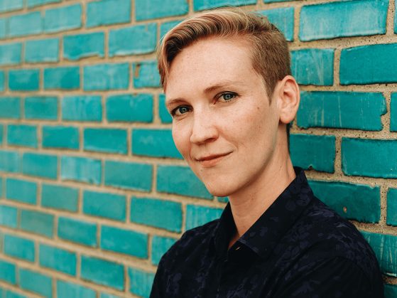 Professor Renée Jørgensen is dressed in a black shirt and standing in front of a light blue wall.
