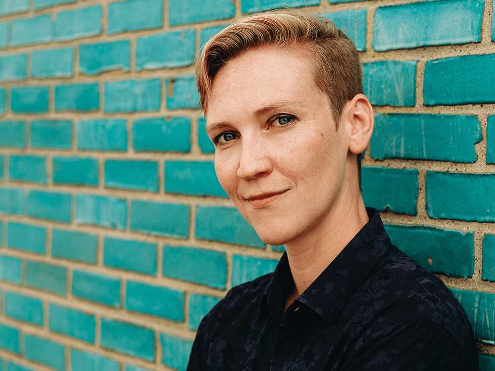 Professor Renée Jørgensen is dressed in a black shirt and standing in front of a light blue wall.