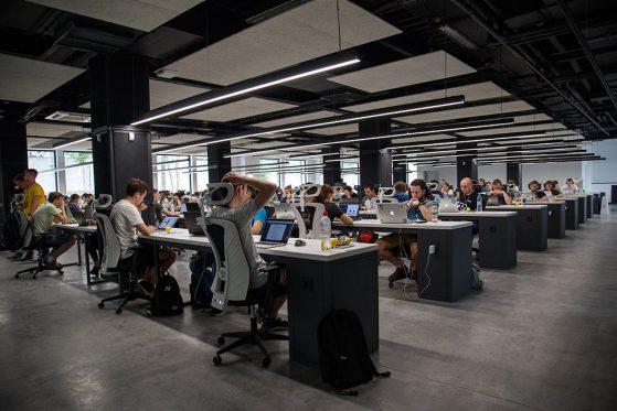 A photograph of a large office with rows of people staring at laptop computers.