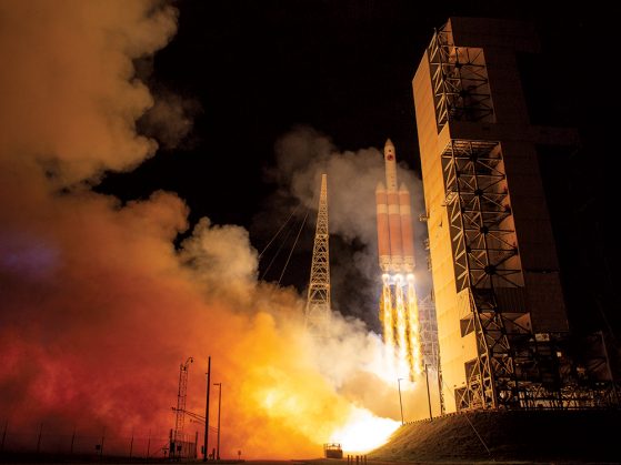 A photograph of the launch of the Parker Solar Probe. A chain of fire extends from the rocket to the earth and red and yellow billowing plumes of smoke drift up around it.