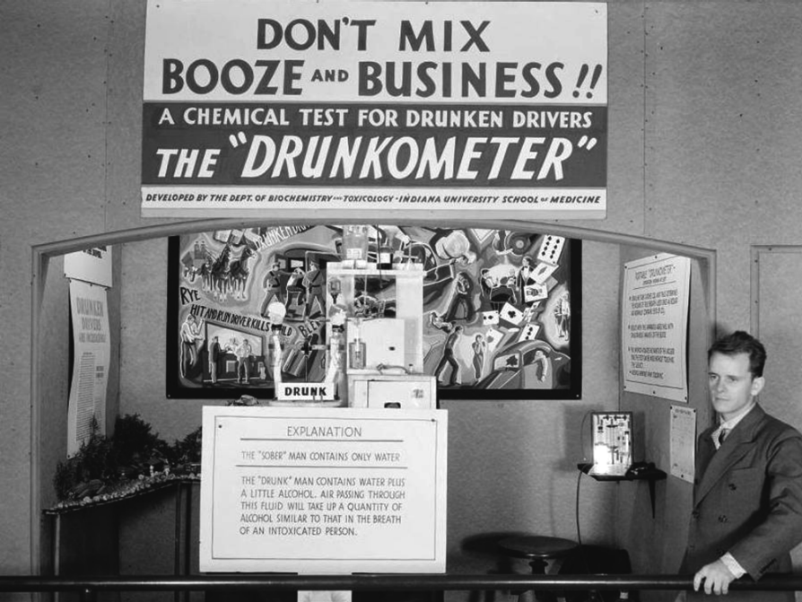 A man stands off to the side of what looks like a booth advertising the new "drunkometer" invention. He's surrounded by lots of informational signs. The largest of them all, above the booth, says, "Don't mix booze and business!! A chemical test for drunken drivers: the 'Drunkometer'. Developed by the dept. of biochemistry and toxicology, Indiana University School of Medicine."