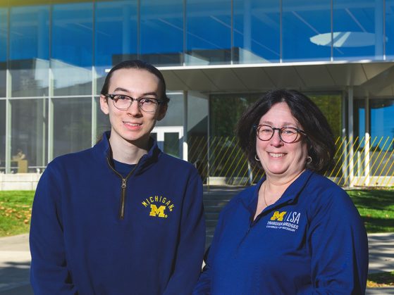 Alan and Linda, a son and mother in blue U-M gear, stand in front of the LSA building at the University of Michigan on a sunny day.