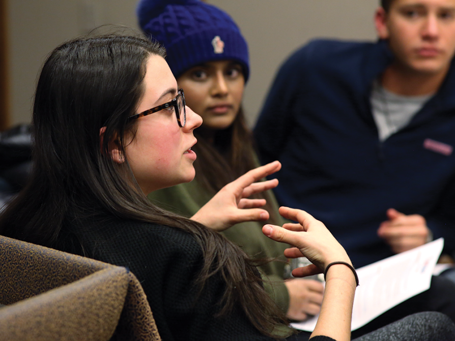 A woman is talking and gesturing with her hands. Other students are looking intently at her.