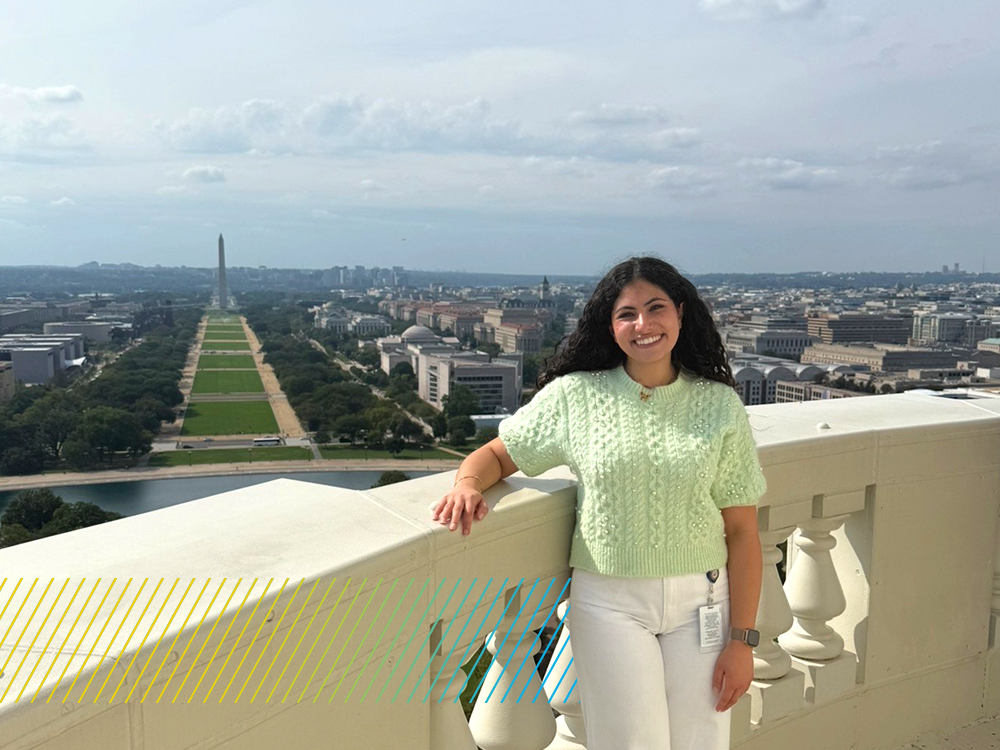 A woman stands on a balcony of the U.S. Capitol with the National Mall in the background.