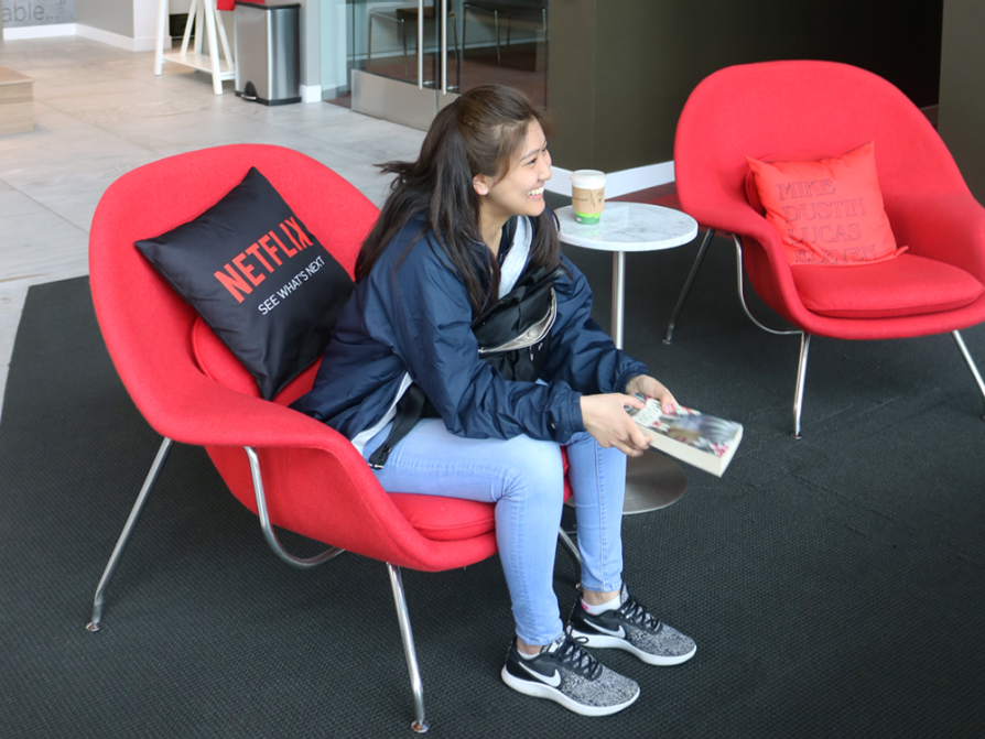 A beaming student who is sitting on a bright red chair. A black throw pillow behind her says Netflix.