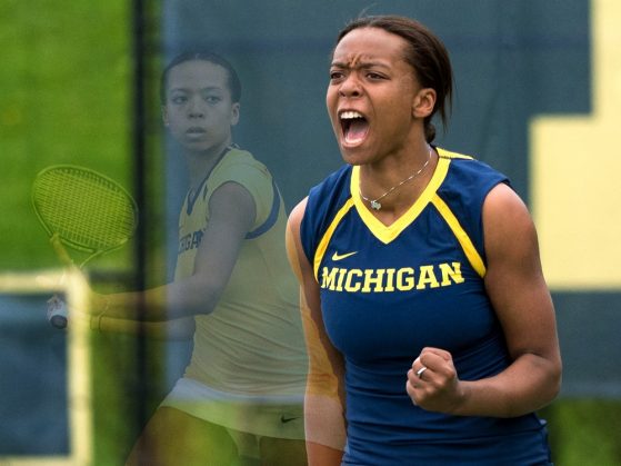 Brienne Minor on a tennis court wearing her blue U-M tennis team uniform, clenching her left fist, and exclaiming in a moment of victory.