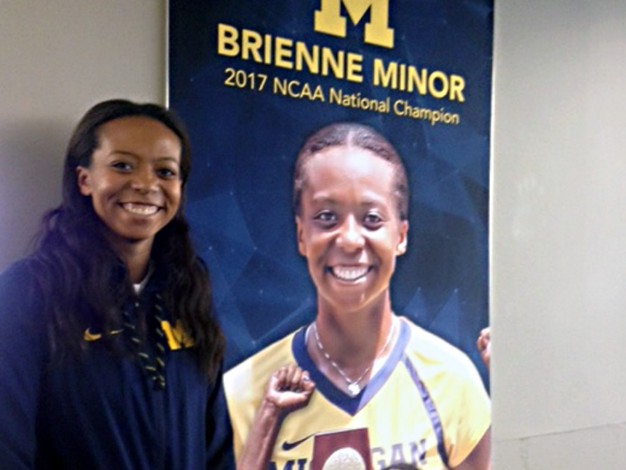 Brienne Minor standing next to the U-M tennis banner that bears her photograph.