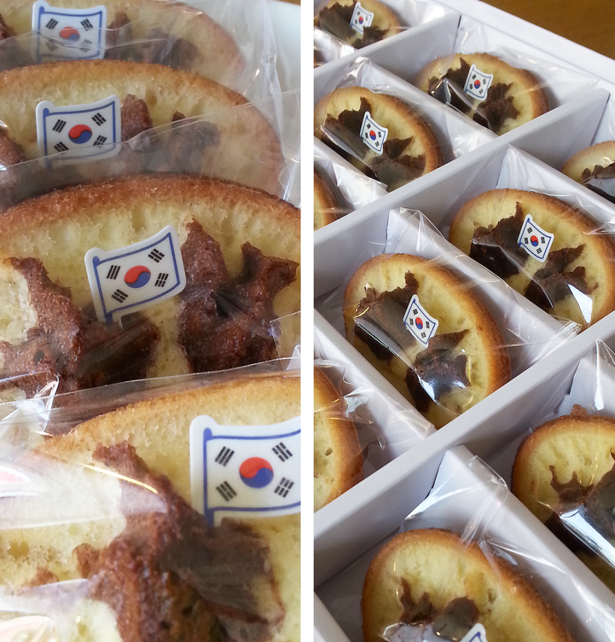 Dokdo bread in packaging tray. On the individual pieces of bread, the dark outline of the islands is visible against the lighter part. A Korean flag is planted in the brad islands.