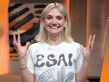 A woman wearing a white T-shirt that says "ESAI" smiles and holds her hands in the air.