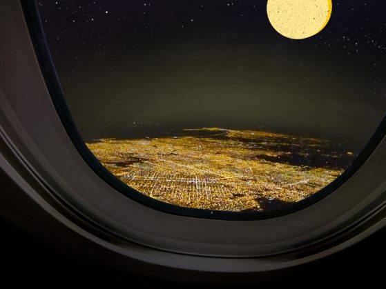 A nighttime view of an illuminated city from an airplane window.