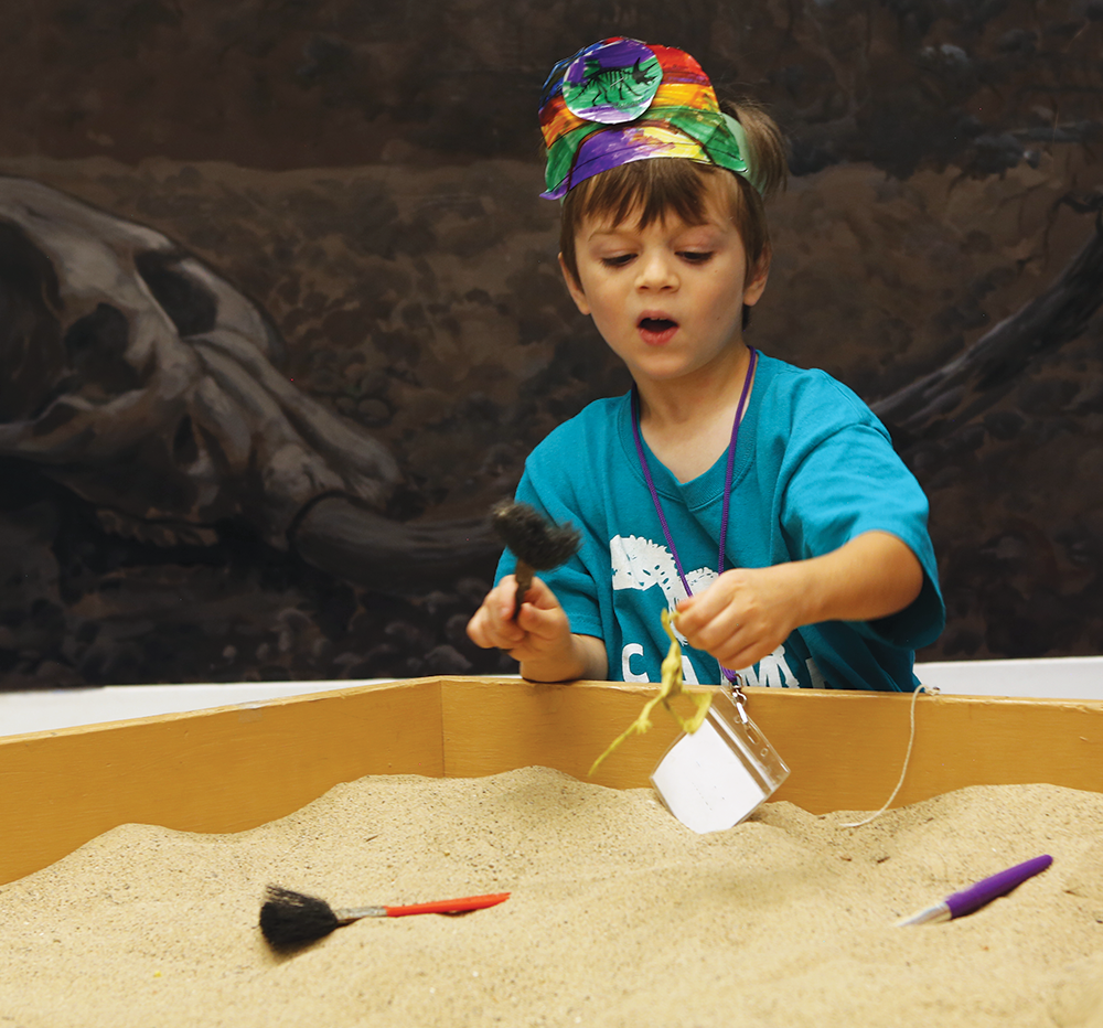 A small child looks for fossils in sand.
