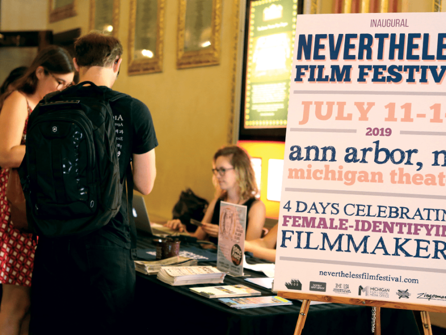 A photograph of people standing at the table in front of a table at the Nevertheless Film Festival.