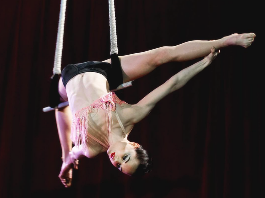 Jones-Rooy is draped over a trapeze reaching back toward her ankles while her legs are in a splits position.