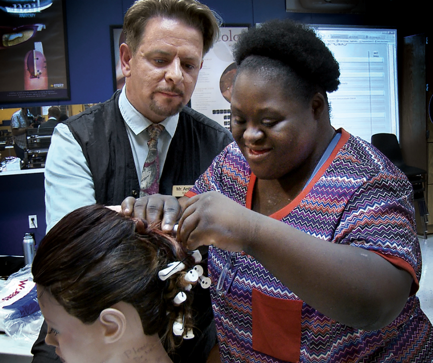 Naomie Monplaisir works on a manequin's hair while her teacher looks on.
