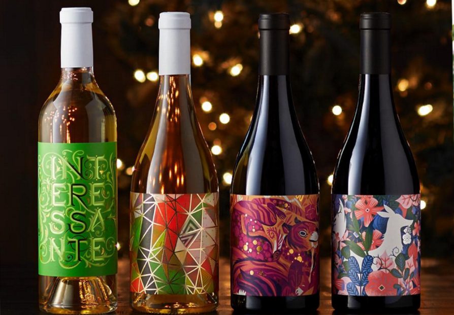 Four wine bottles with a background of small white lights. The two bottles on the left are white wines. The two on the right are red wines. All of the labels have patterns of bright, vibrant colors.