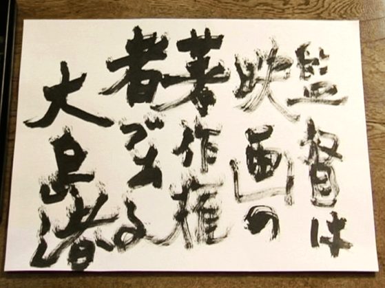 A film still of a white piece of paper, on which is calligraphic writing in black ink. From left to right, the brushstroke loses its intensity.