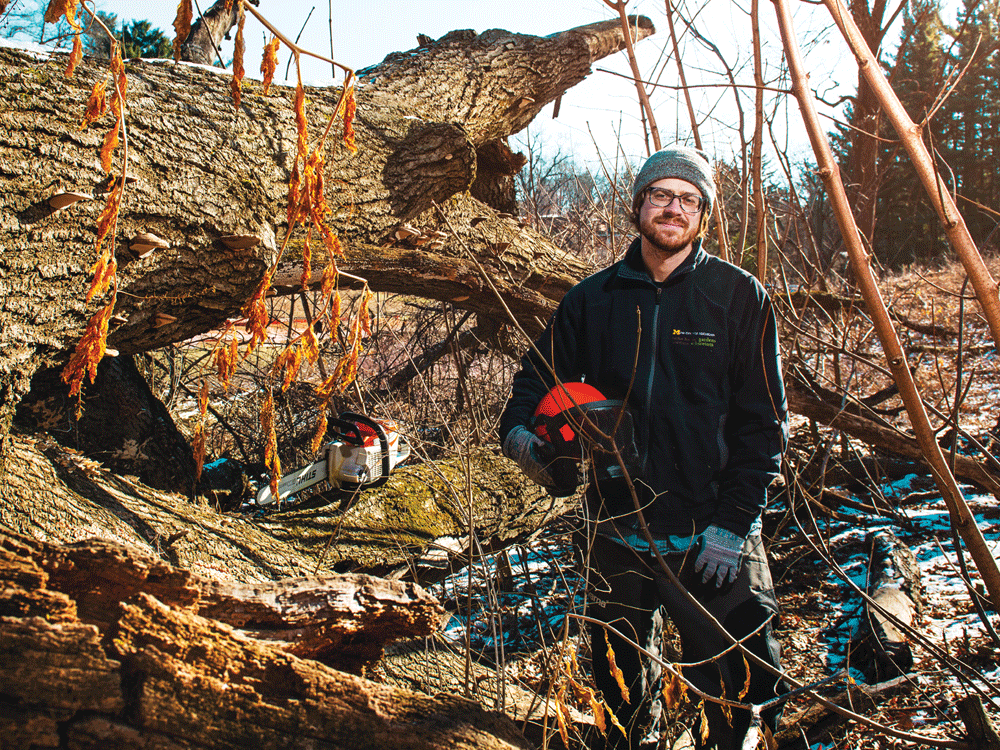 Alum Chad Machinski stands with a tree and a chainsaw in The Arb.