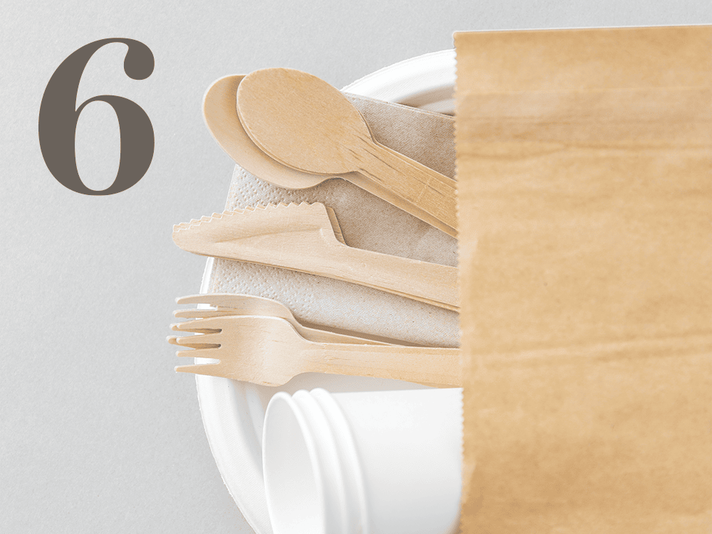 Compostable utensils, cups, napkins, and a plate stick out of a paper bag next to a stylized numeral 6.