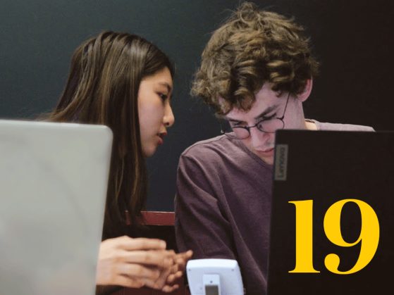 Two students lean in to consult quietly with each other. A stylized numeral 19 is also pictured. 