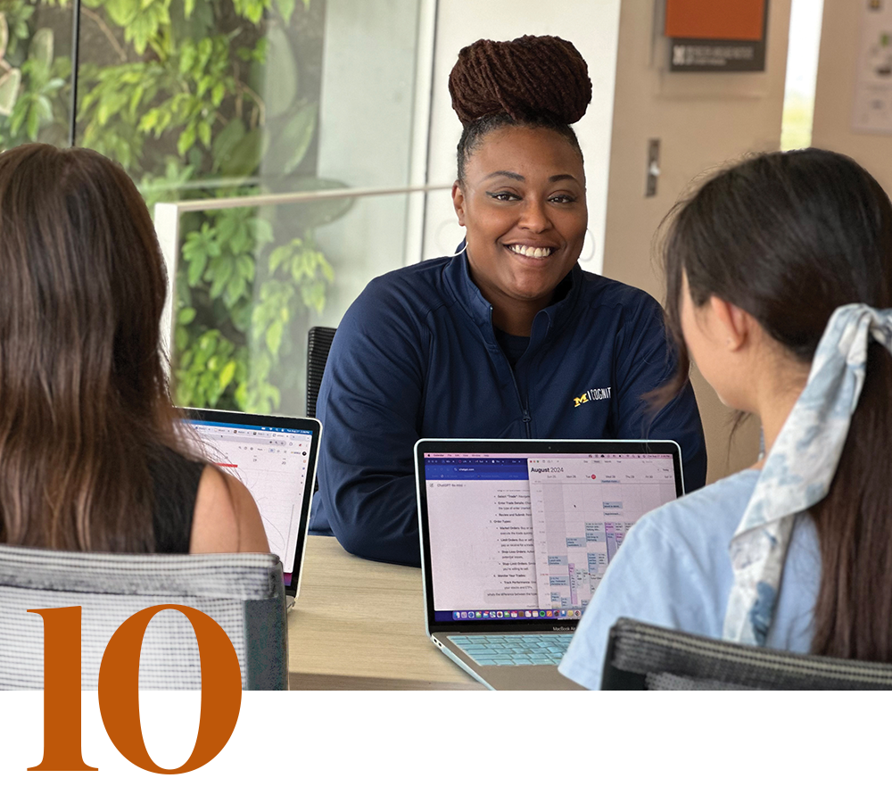 A person facing the camera advises two undergraduate students with their laptops open and their backs to the camera, alongside a stylized numeral 10.