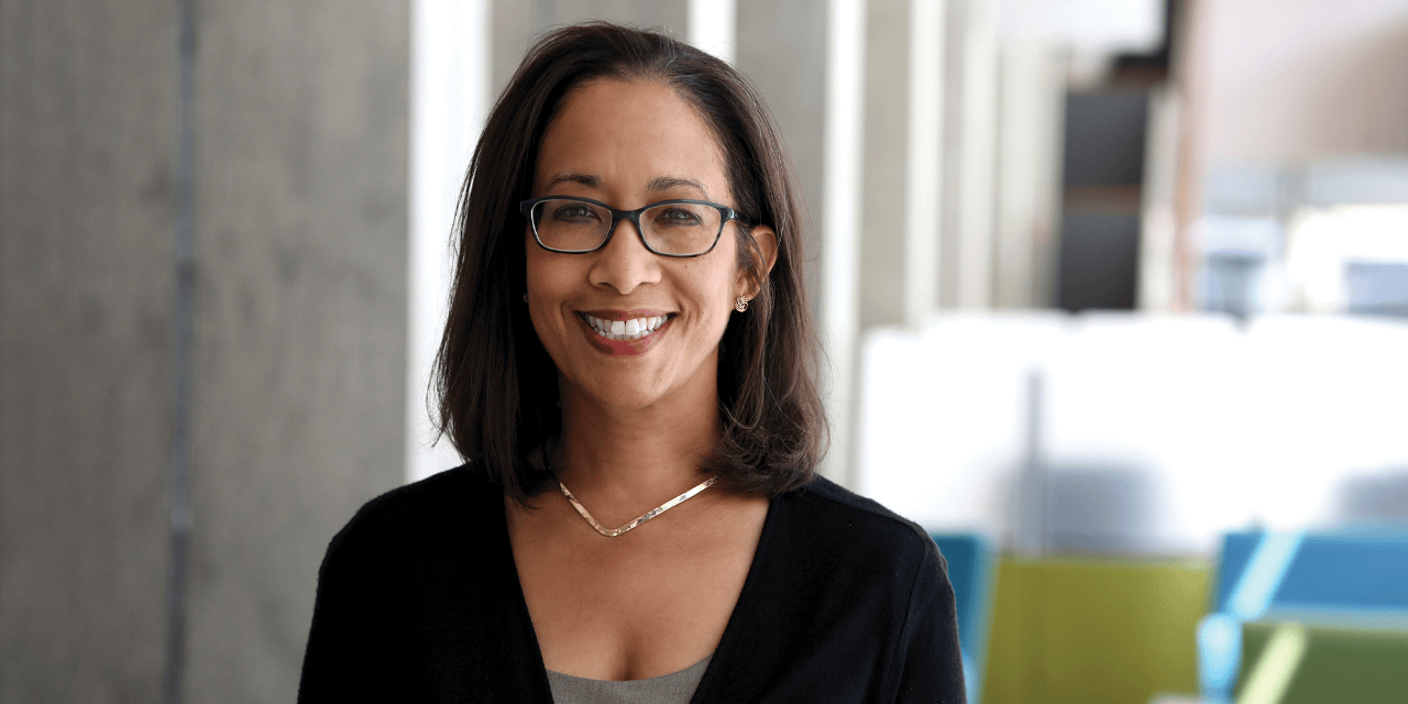 A photographic portrait of Rosie Ceballo, wearing glasses and smiling.