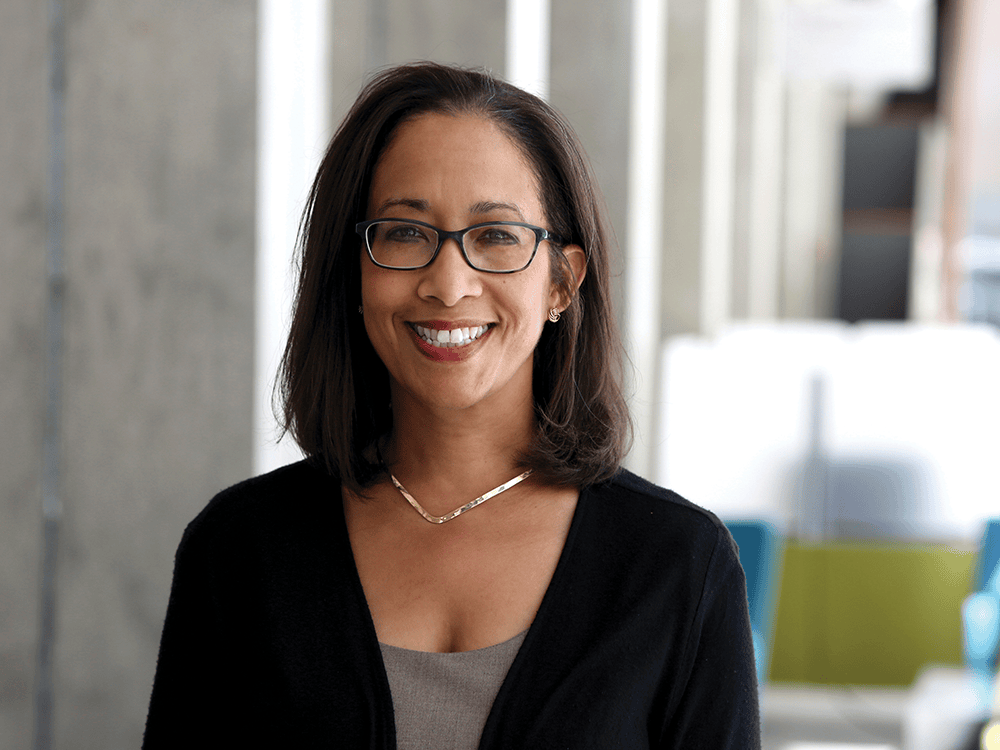 A photographic portrait of Rosie Ceballo, wearing glasses and smiling.